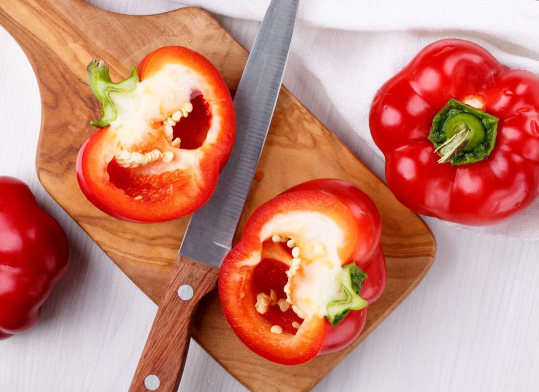 red bell pepper cut in half on cutting board with knife
