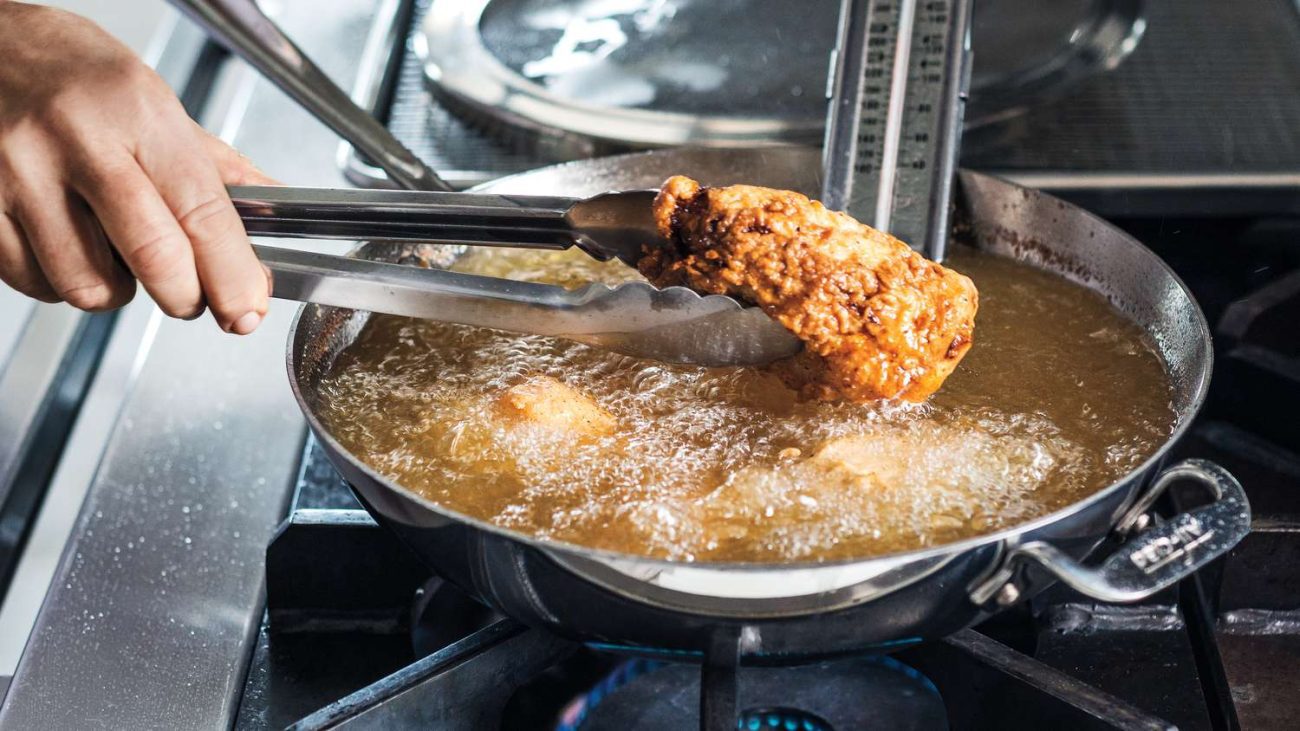 tongs holding fried chicken over a pan of oil