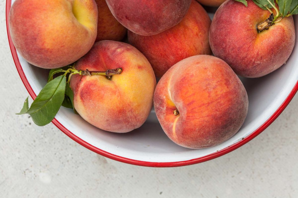 fresh peaches in white metal bowl with red rim