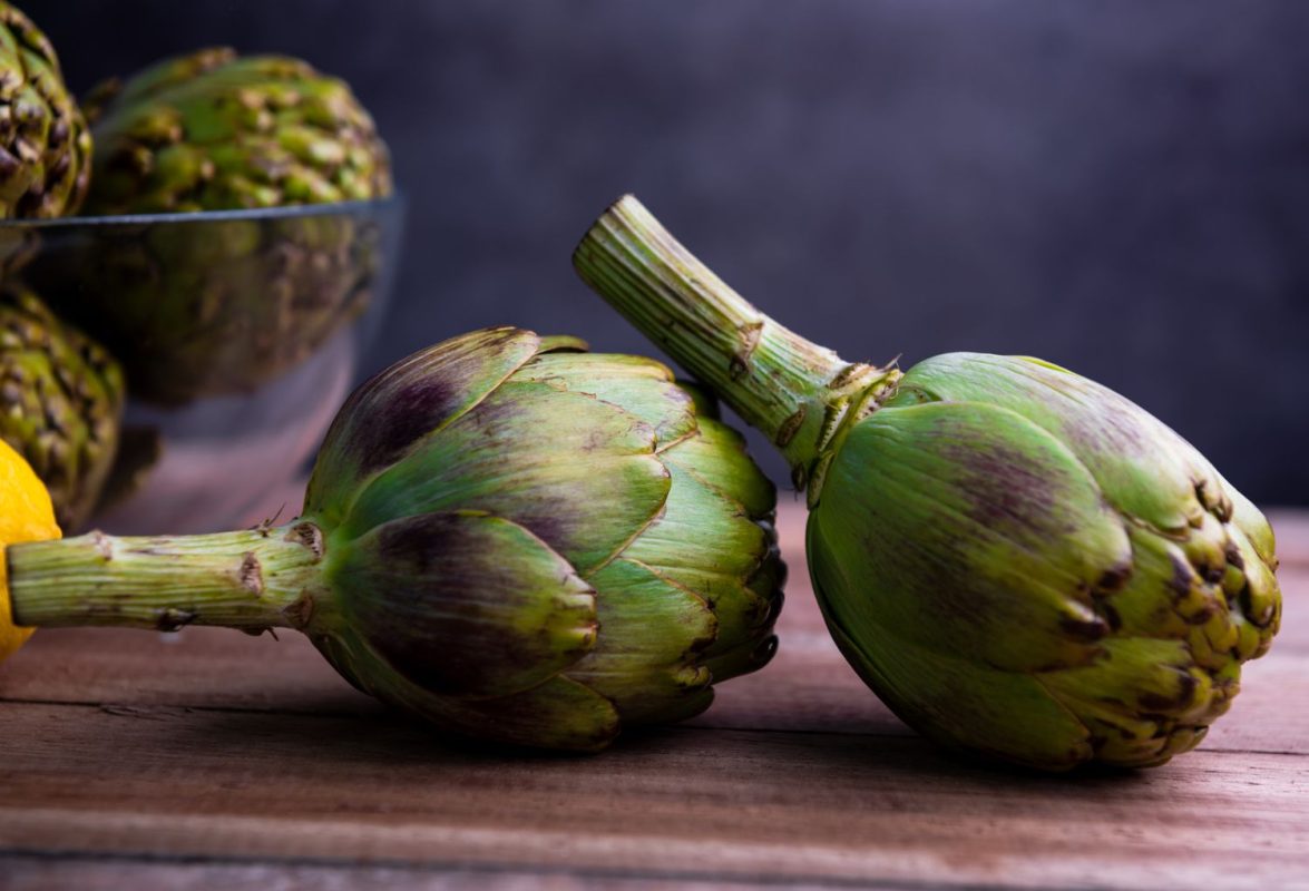 side view of two artichokes on wood surface