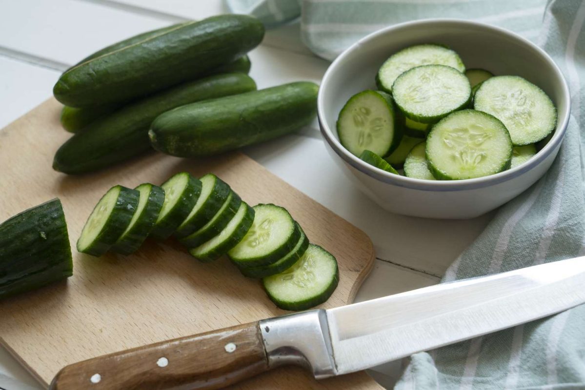 sliced and whole cucumbers on a chopping board and in a bowl