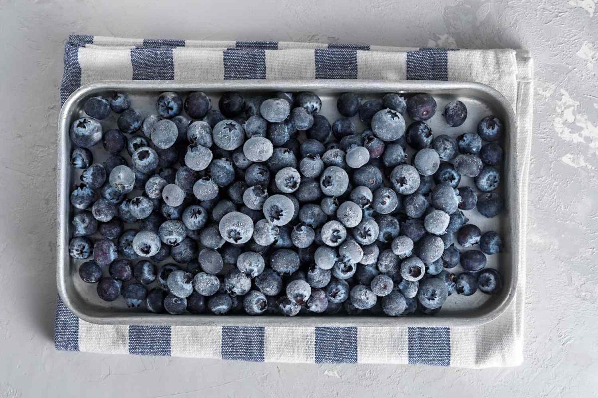 frozen blueberries on a baking sheet with a striped kitchen cloth underneath