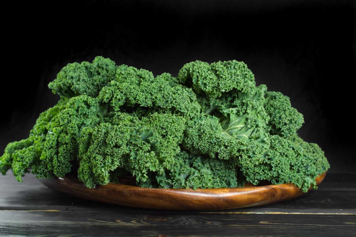 kale leaves in shallow wooden bowl with dark background