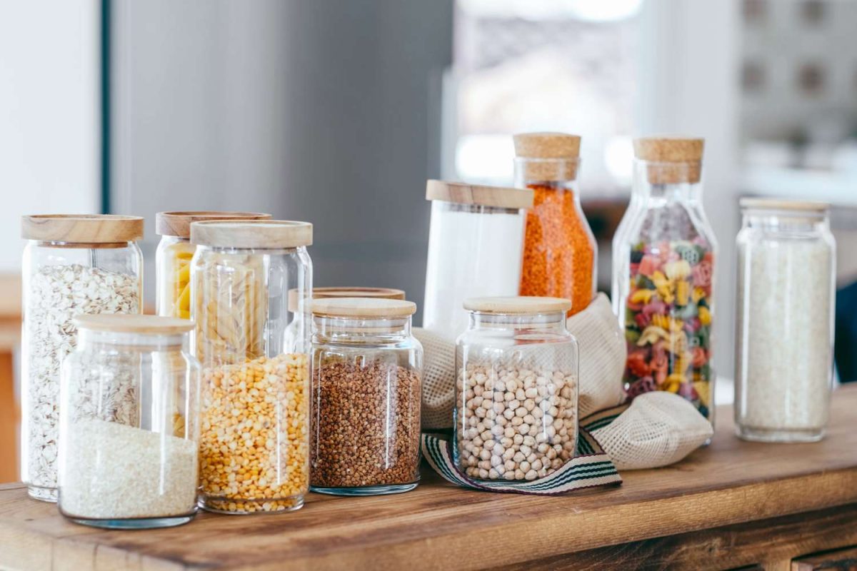 Various jars with grains legumes and food items displayed on a wooden surface