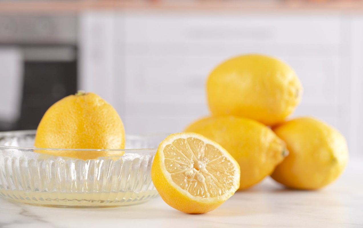 lemon being juiced in glass manual juicer and more lemons on marble counter