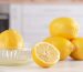 lemon being juiced in glass manual juicer and more lemons on marble counter