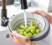 Someone washing grapes in a colander under a faucet