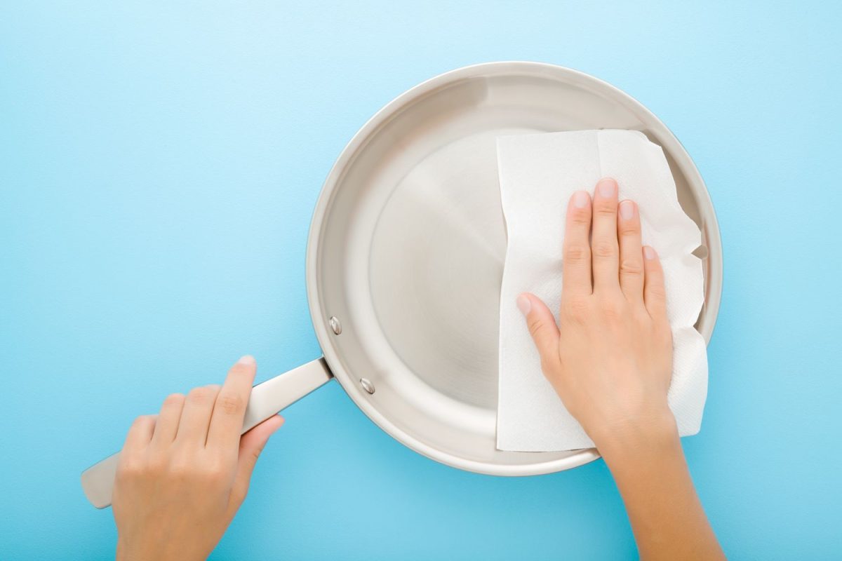 A hand cleaning a frying pan with a paper towel