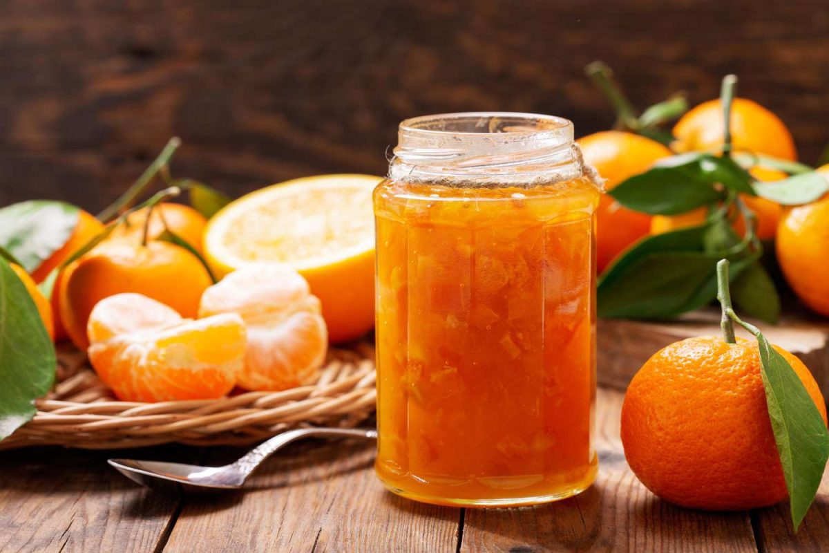 Jar of marmalade surrounded by oranges and a spoon