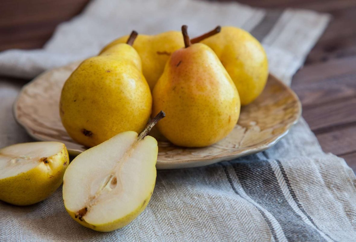 A plate with whole pears and a halved pear on a clothcovered surface