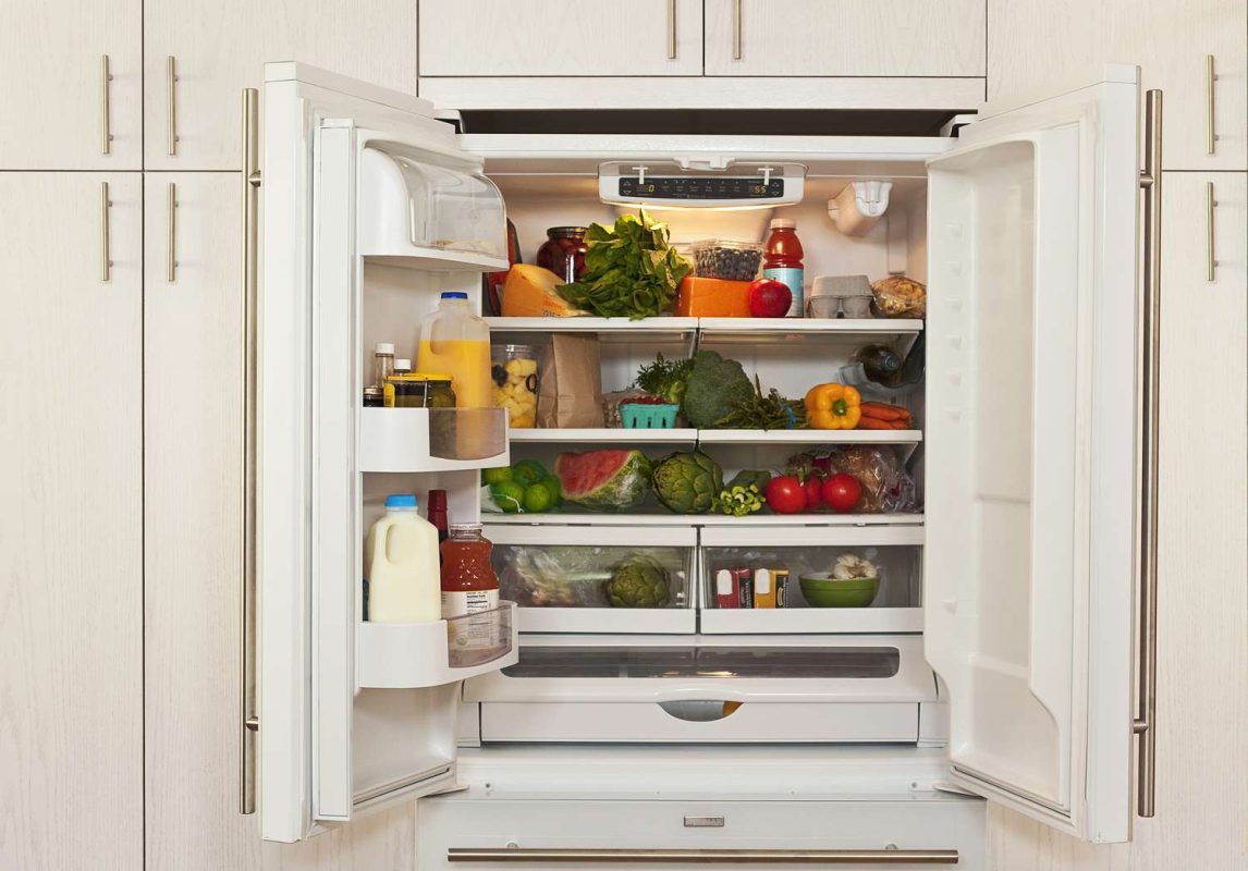 Refrigerator with open doors showing shelves stocked with various fresh produce and packaged food items
