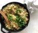 A skillet containing cooked quinoa garnished with fresh herbs and a wooden spoon placed within